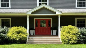 A two-story house with a red front door, a porch with white columns, and a small front yard with bushes. - Mountain Views, Playroom, Fireplaces, Sleeps 8+! (Great Barrington)