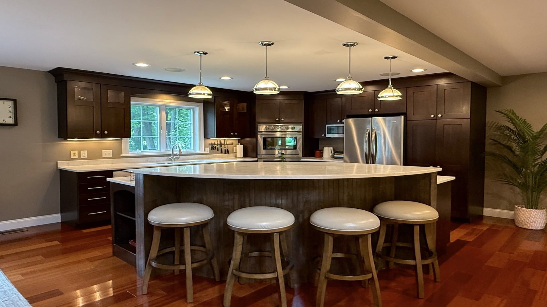 Une cuisine moderne dotée d’un grand îlot central, de tabourets de bar, d’appareils électroménagers en acier inoxydable et de luminaires suspendus.