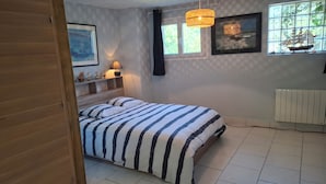 Une chambre à coucher avec un lit, une fenêtre avec des rideaux, un radiateur et une étagère ornée d’objets décoratifs.