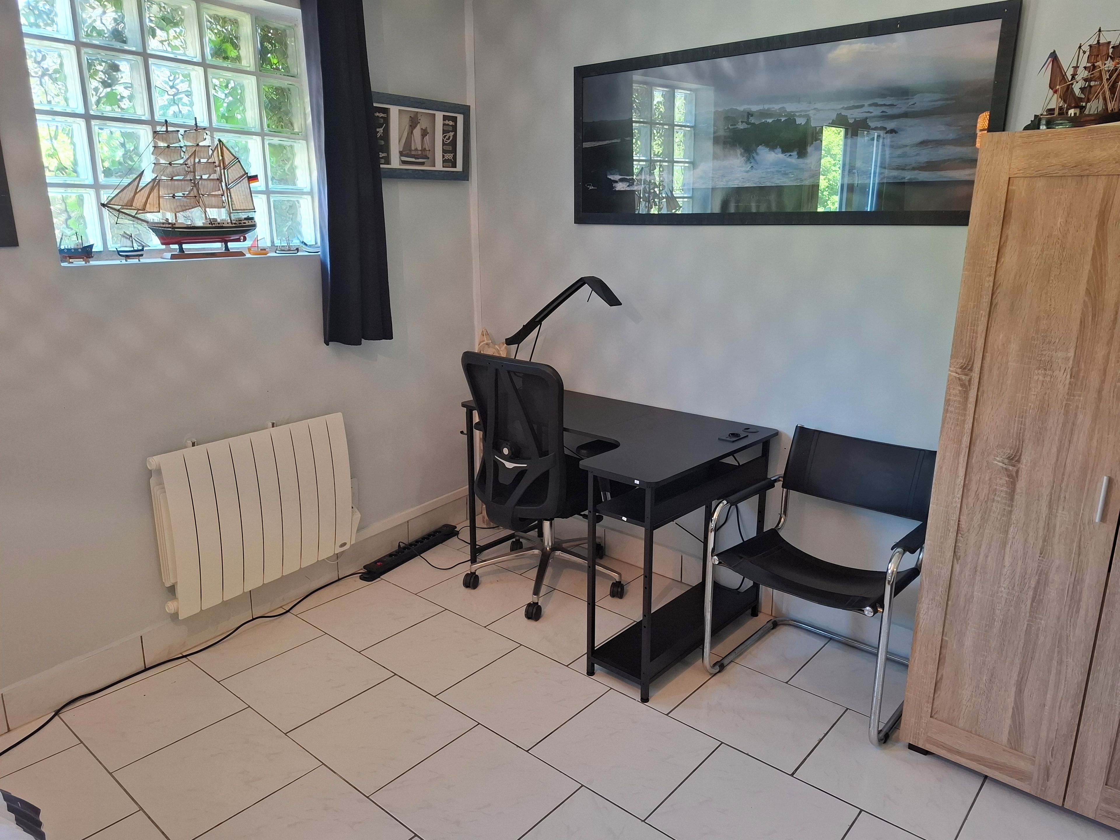 Ein Zimmer mit Schreibtisch, Stuhl, Heizkörper und Schrank.