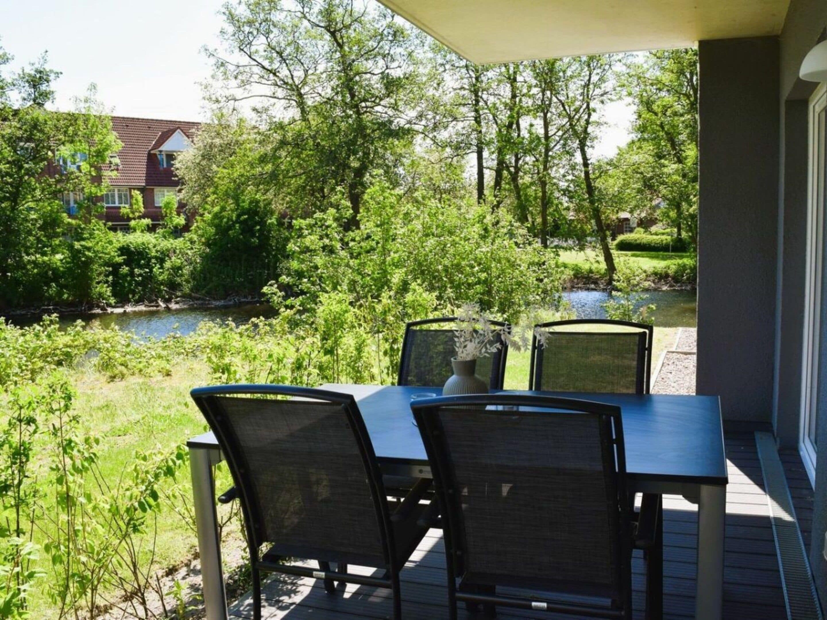 Eine Terrassensitzgelegenheit im Freien mit Tisch und Stühlen, mit Blick auf ein Gewässer und Grünflächen.