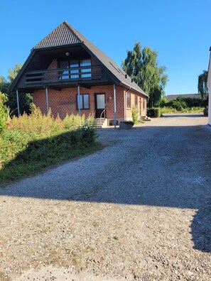 Ein eingeschossiges Backsteingebäude mit geneigtem Dach, einer Veranda und einer Schotterauffahrt zum Eingang.