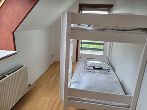 Ein Mehrbettzimmer mit Holzboden, weißen Wänden und einem Fenster mit Jalousien.