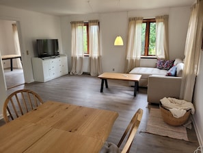 Ein modernes Wohnzimmer mit einem Holzesstisch, einer Couch, einem Fernseher und einem Fenster mit Vorhängen.