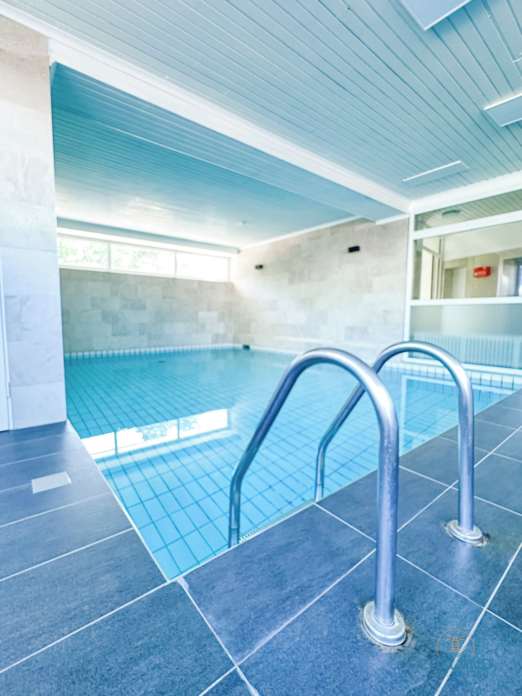Ein Schwimmbecken mit hellblauen Fliesen, Metallhandläufen und einem gefliesten Boden.
