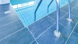 En swimmingpool med klare blå fliser, metalgelændere og flisebelagt gulv.