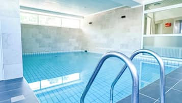 Ein Schwimmbecken mit hellblauen Fliesen, Metallhandläufen und einem gefliesten Boden.