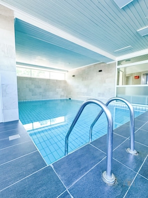 Ein Schwimmbecken mit hellblauen Fliesen, Metallhandläufen und einem gefliesten Boden.