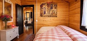 A cozy wooden room with a bed, a dresser, a mirror, and a wall with a floral mural.