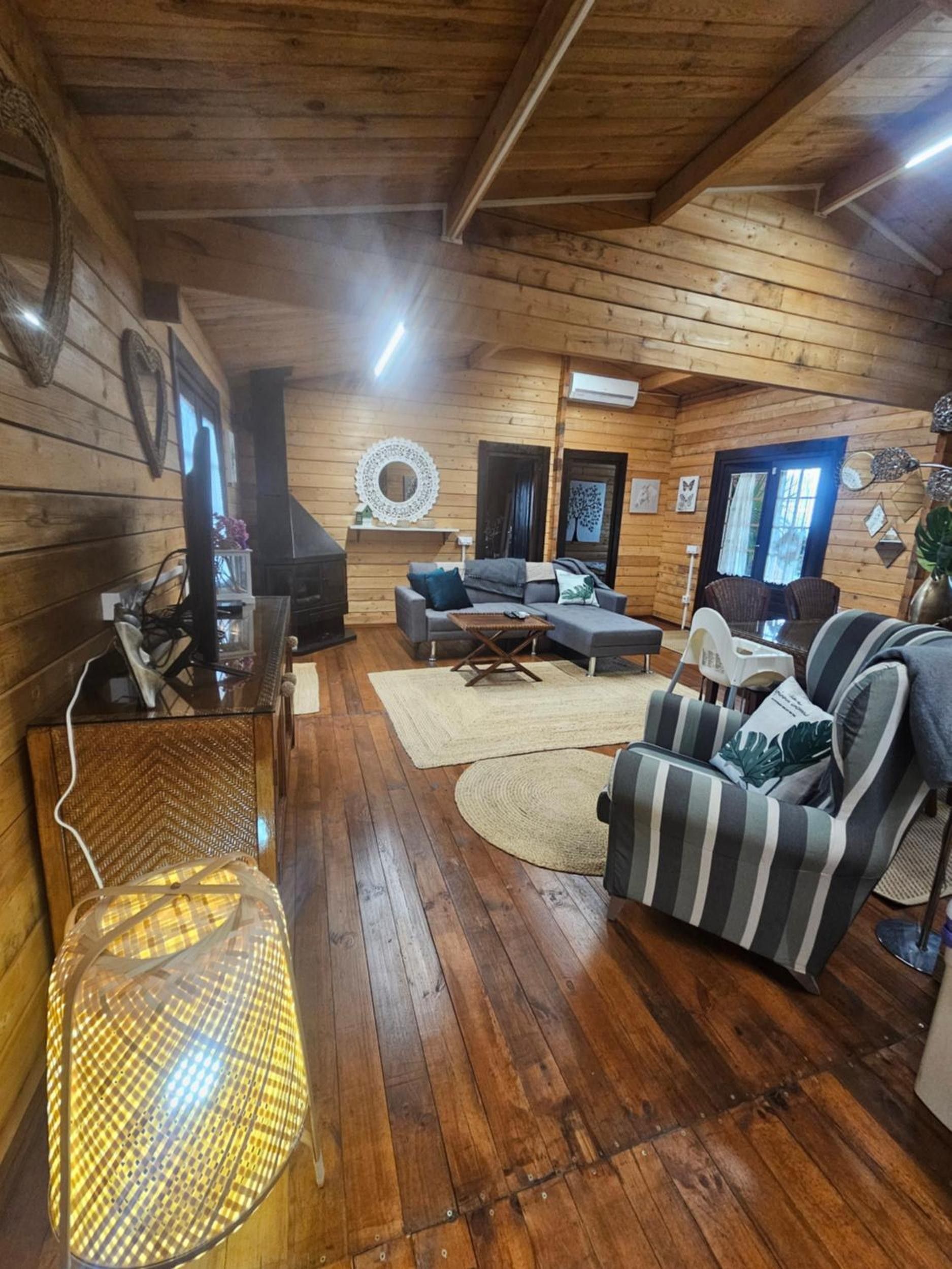 Een gezellig chaletinterieur met houten wanden, een bank, een gestreepte fauteuil, een televisie en een decoratieve spiegel.