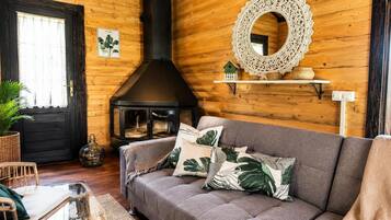 A cozy living room with a fireplace, a sofa with decorative pillows, wicker furniture, and a wooden wall with a decorative mirror.