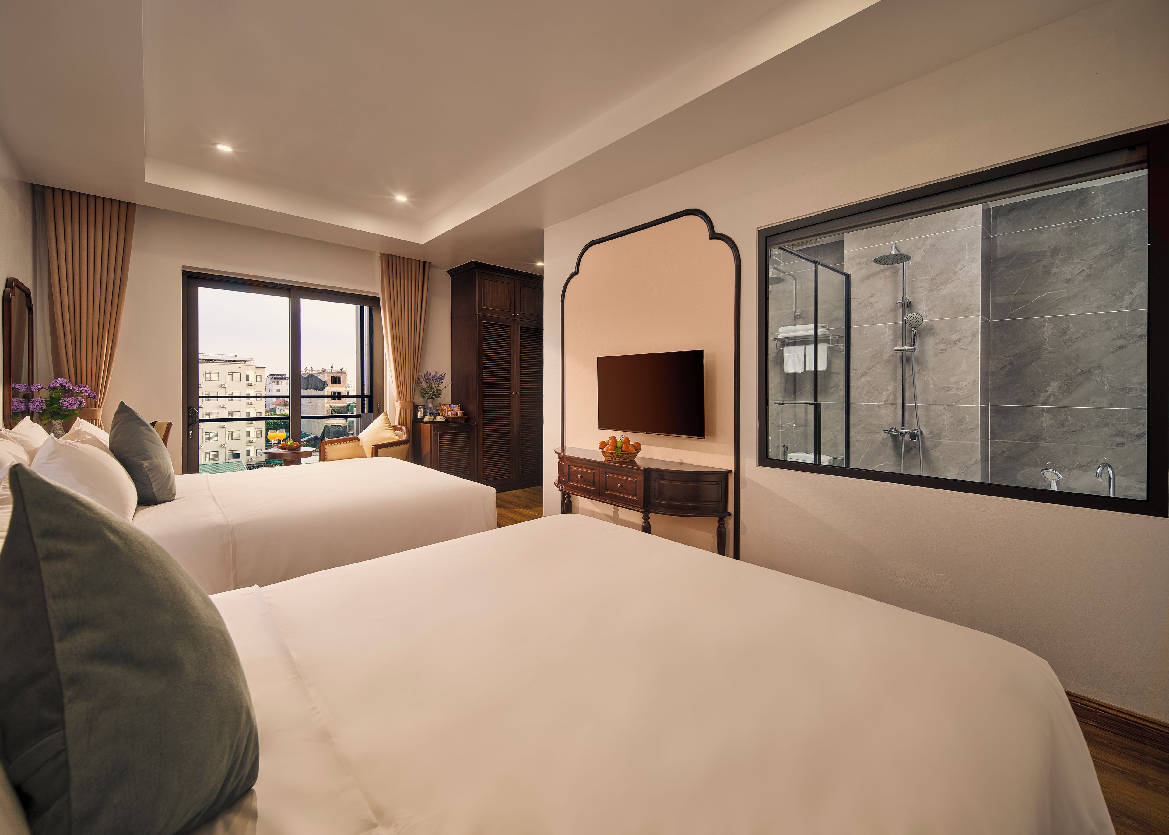 Habitaci ón de hotel con dos camas, televisión, baño con ducha y vista a edificios.