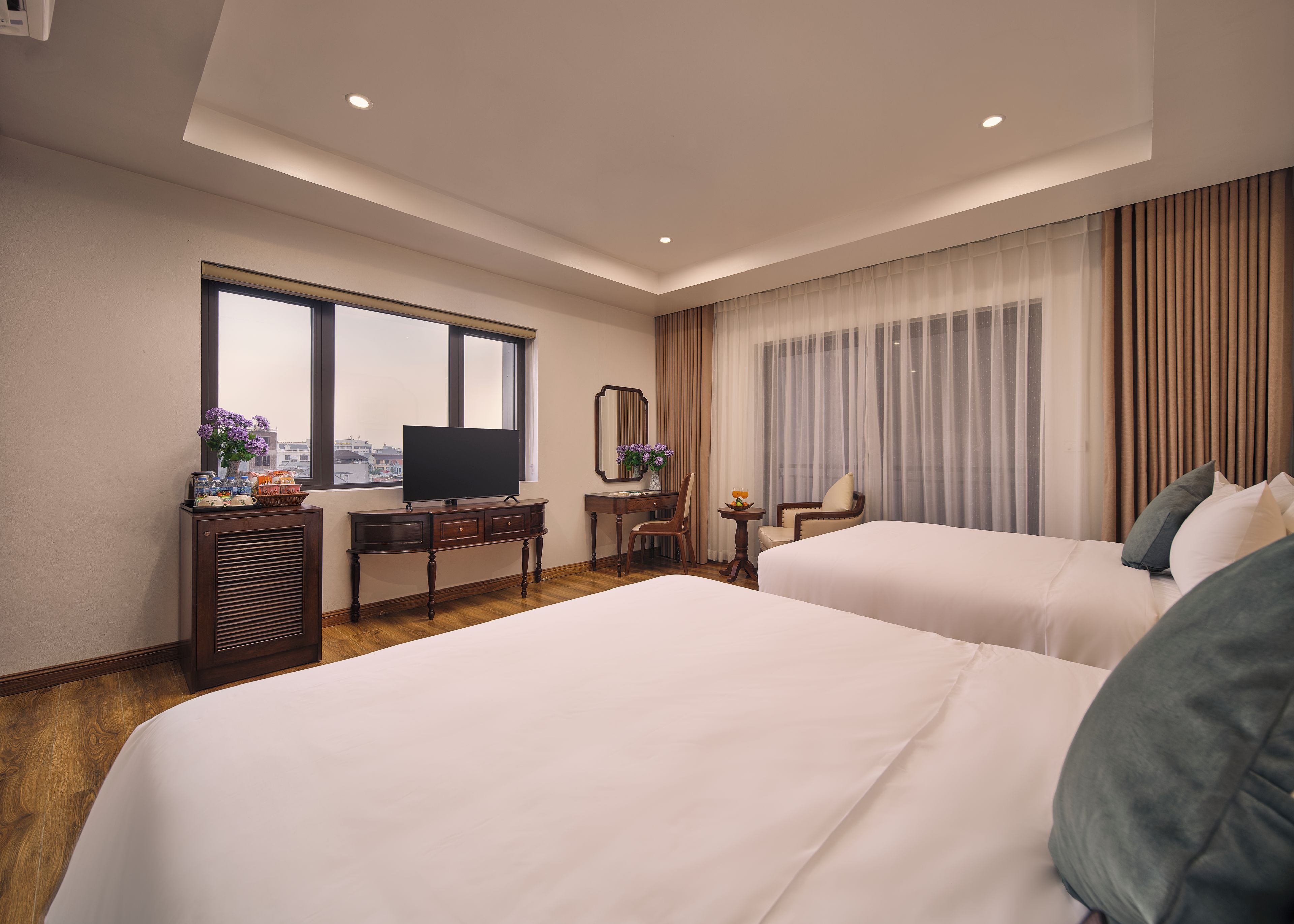 A hotel room with two beds, a desk with a television, a chair, and a window with curtains.