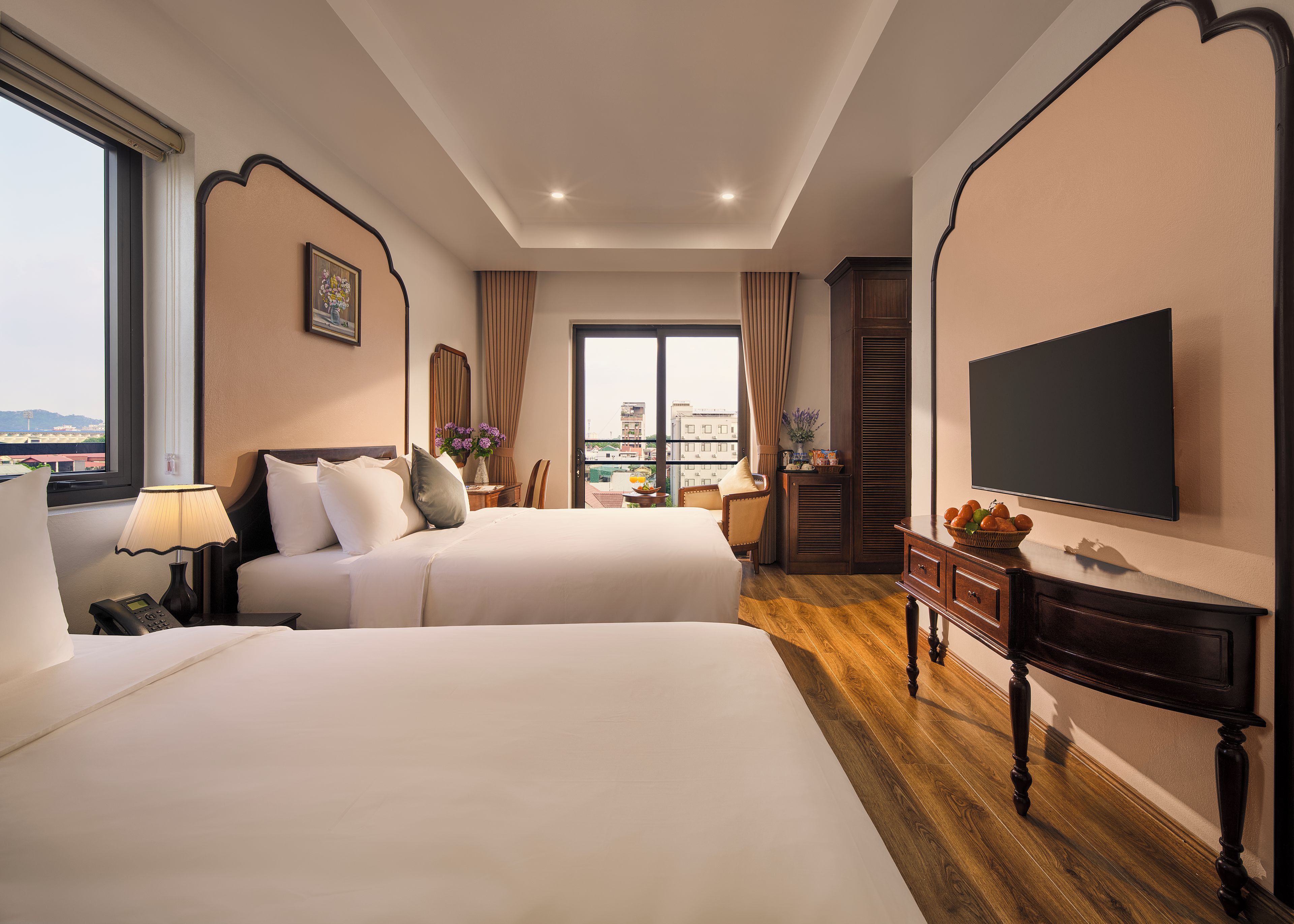 A hotel room with two beds, a desk, a TV, and a balcony with a view.