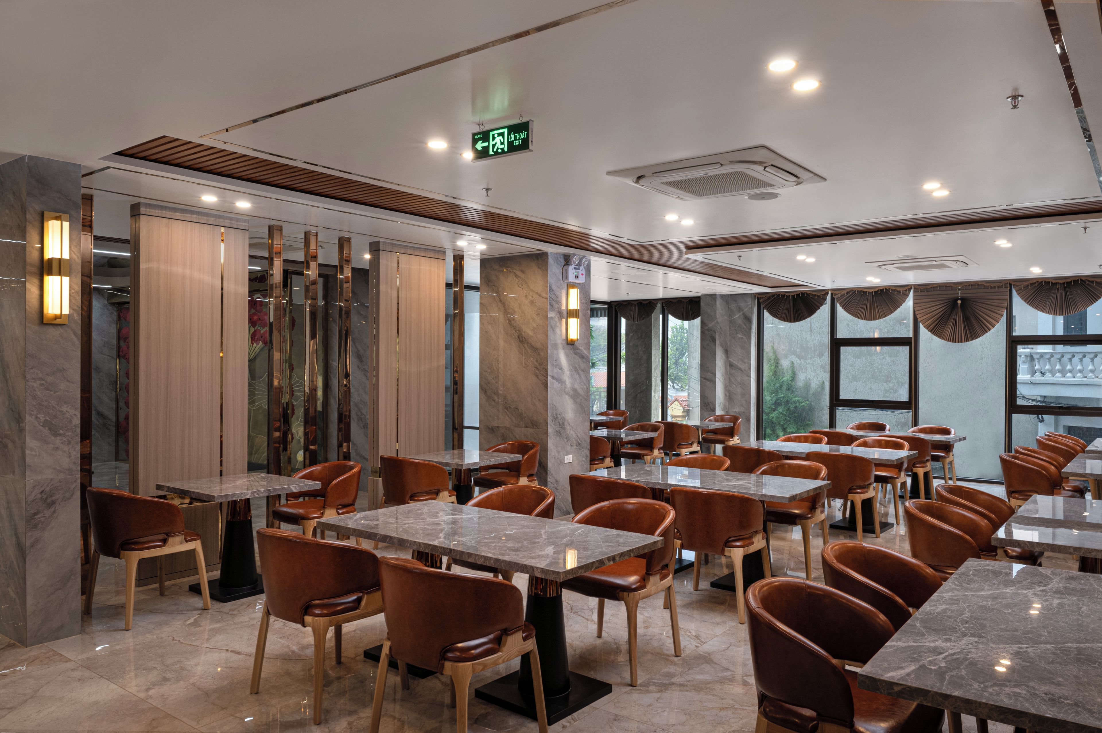 L’intérieur d’un restaurant avec des tables et des chaises en marbre, un plafond doté d’un éclairage encastré et une vue sur l’extérieur grâce à de grandes fenêtres.
