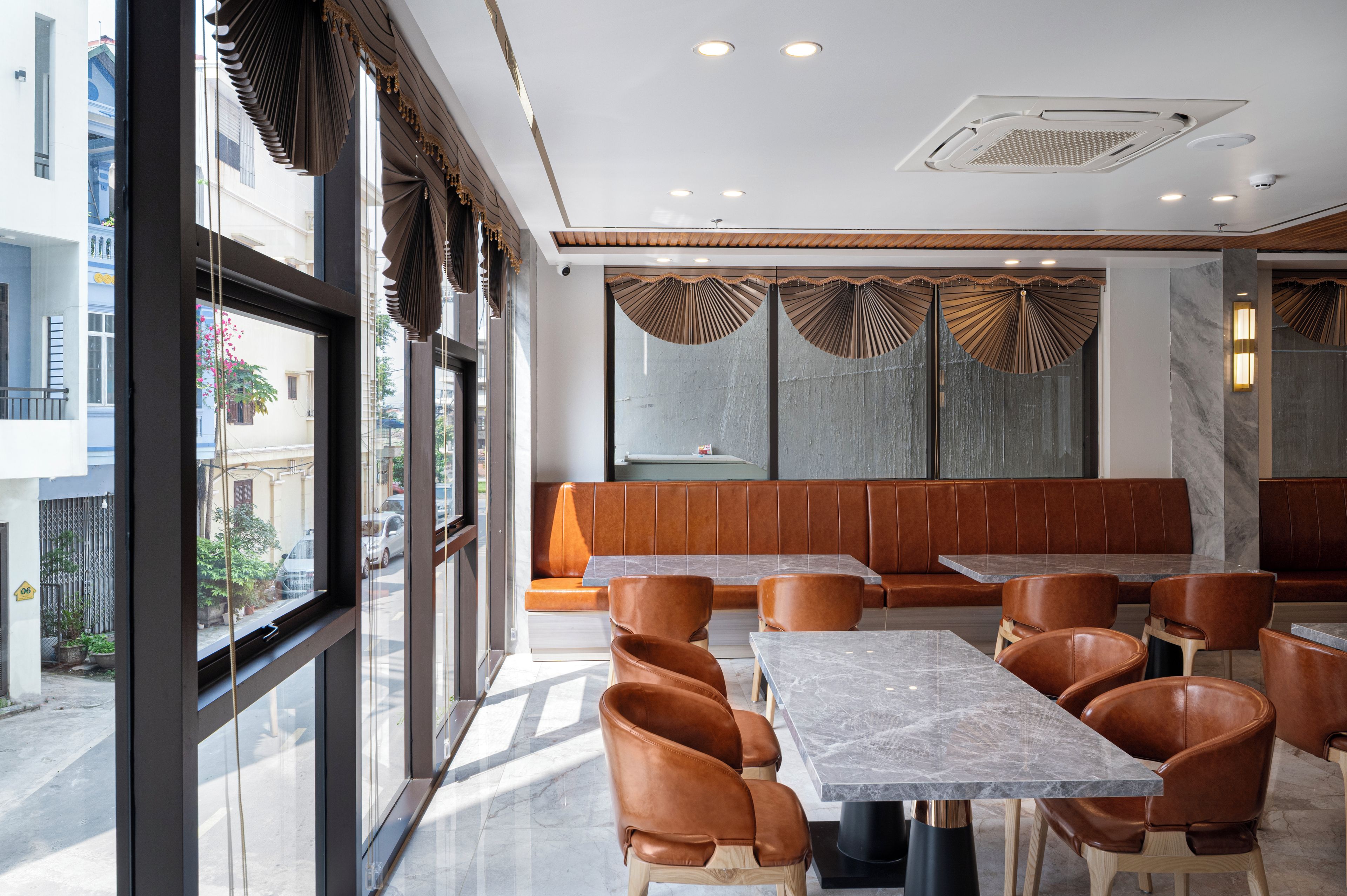 A modern restaurant interior with a long bench seating area, tables, and large windows.