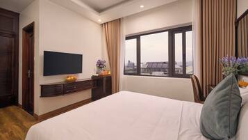 A hotel room with a bed, a flat-screen TV, a window with curtains, and a view of buildings outside.