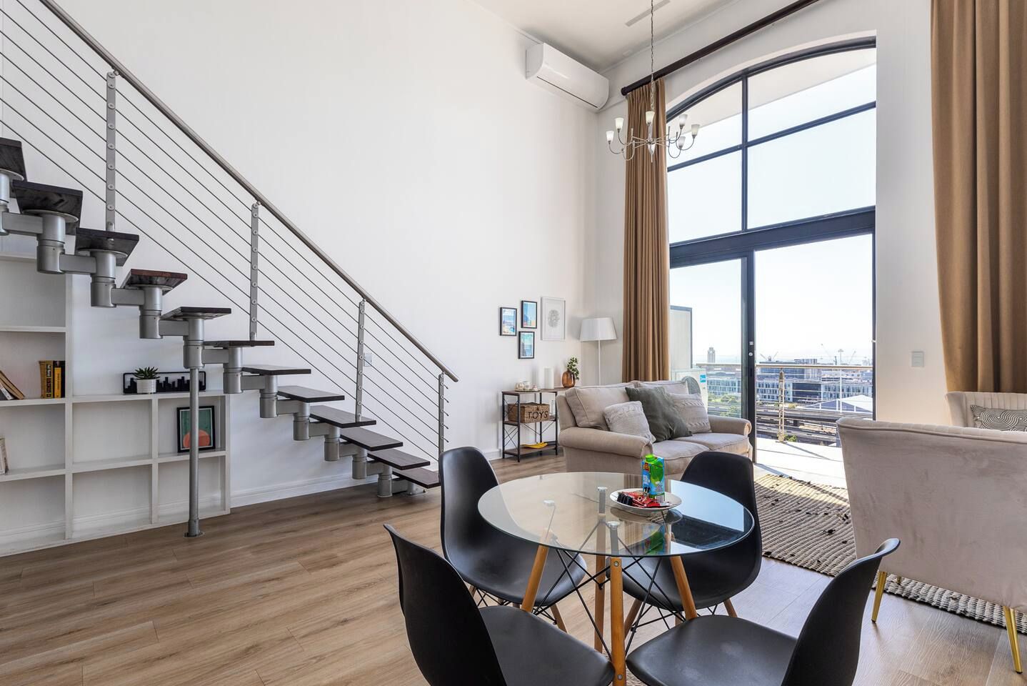 A modern living room with a staircase, a sofa, a coffee table, and a view of the city.