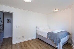 A bedroom with a single bed, a gray and white patterned blanket, and a wooden floor. - Rockwell Penthouse Harbour and City Views by ctha (Cape Town)