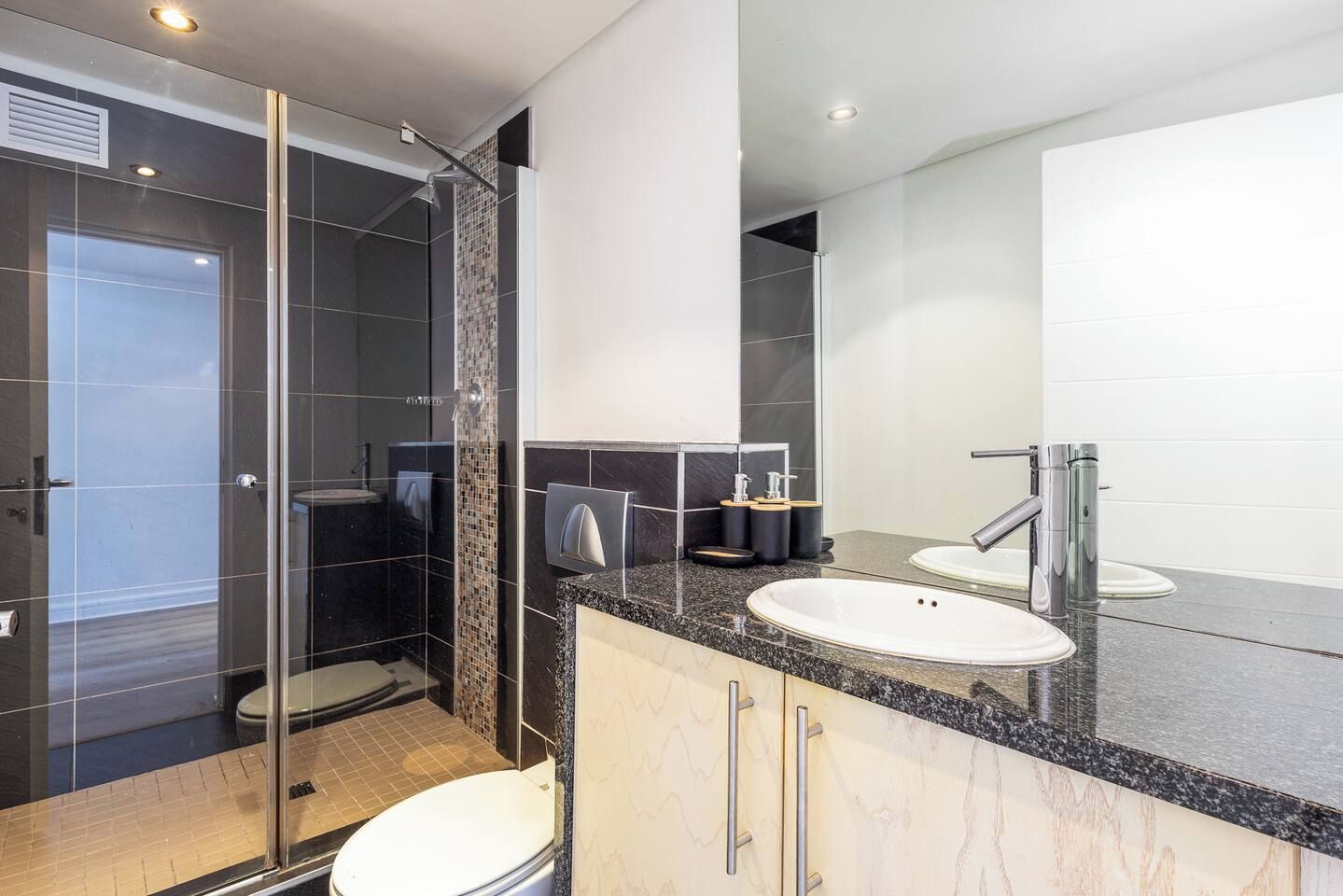Une salle de bain moderne avec une douche à parois de verre, un lavabo blanc et un grand miroir.