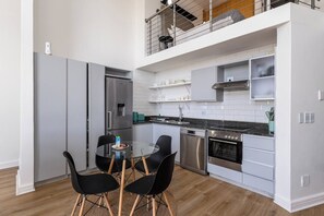 A modern kitchen with a dining table and chairs, stainless steel appliances, and a mezzanine level with a railing. - Rockwell Penthouse Harbour and City Views by ctha (Cape Town)