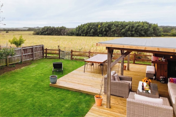A deck with outdoor furniture, a barbecue, and a view of a field.