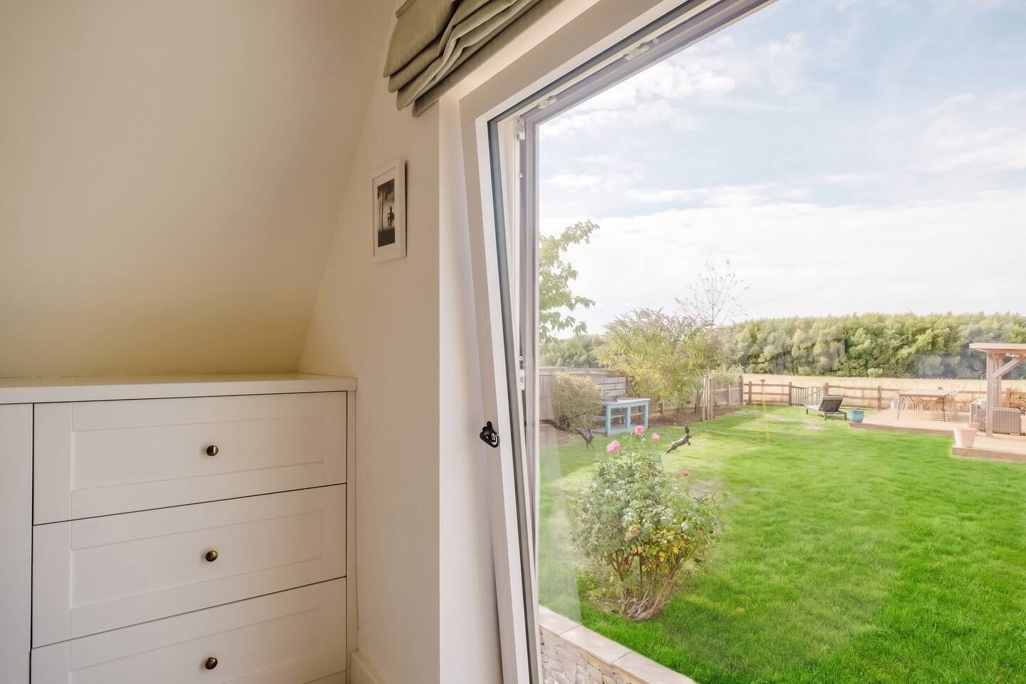 Ein Zimmer mit großem Fenster, weißem Schminktisch und Blick auf einen gepflegten Garten.