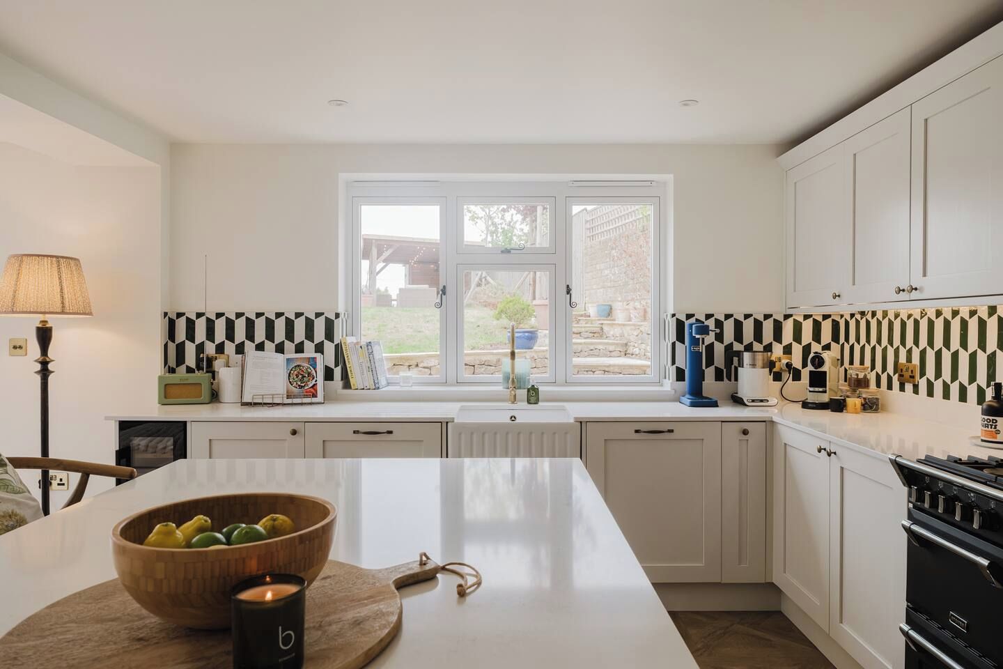 Una cucina moderna con isola centrale, mobili bianchi, una finestra vista e un rivestimento murale decorato.