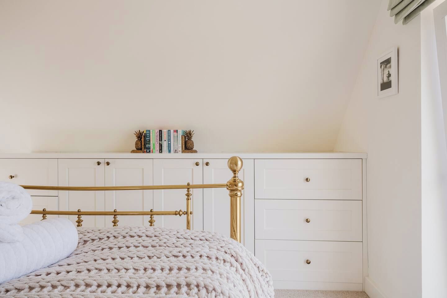 Une chambre à coucher avec un lit, une commode blanche à tiroirs et une étagère avec des livres et des objets décoratifs.