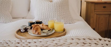 A neatly made bed with a white blanket, a bedside table with a lamp, and a tray with croissants, jam, and orange juice.
