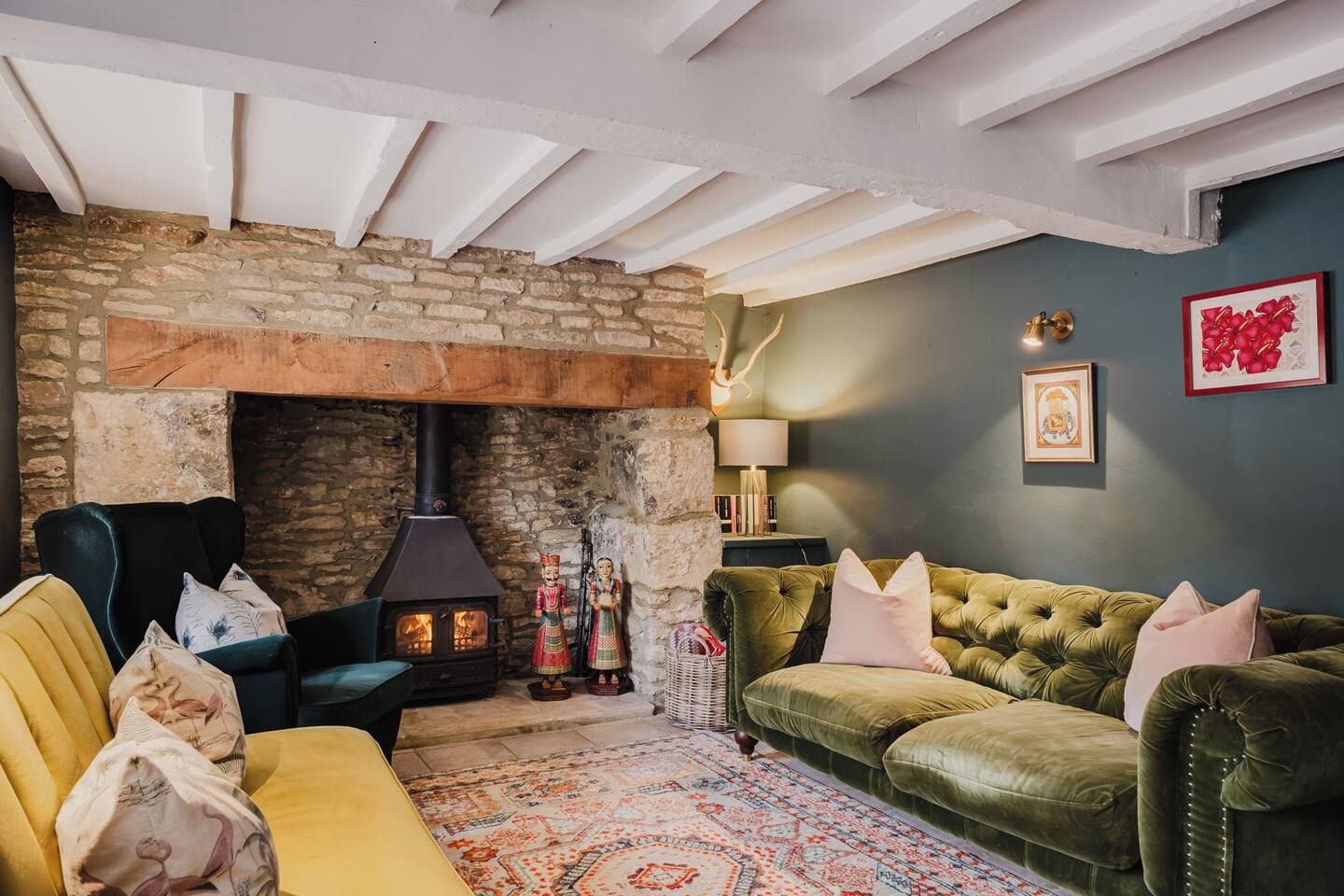 A cozy living room with a stone fireplace, a green sofa, a yellow armchair, and a patterned rug.