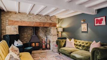 A cozy living room with a stone fireplace, a green sofa, a yellow armchair, and a patterned rug.