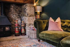 A cozy living room with a stone fireplace, a plush green sofa, and traditional wooden figurines.