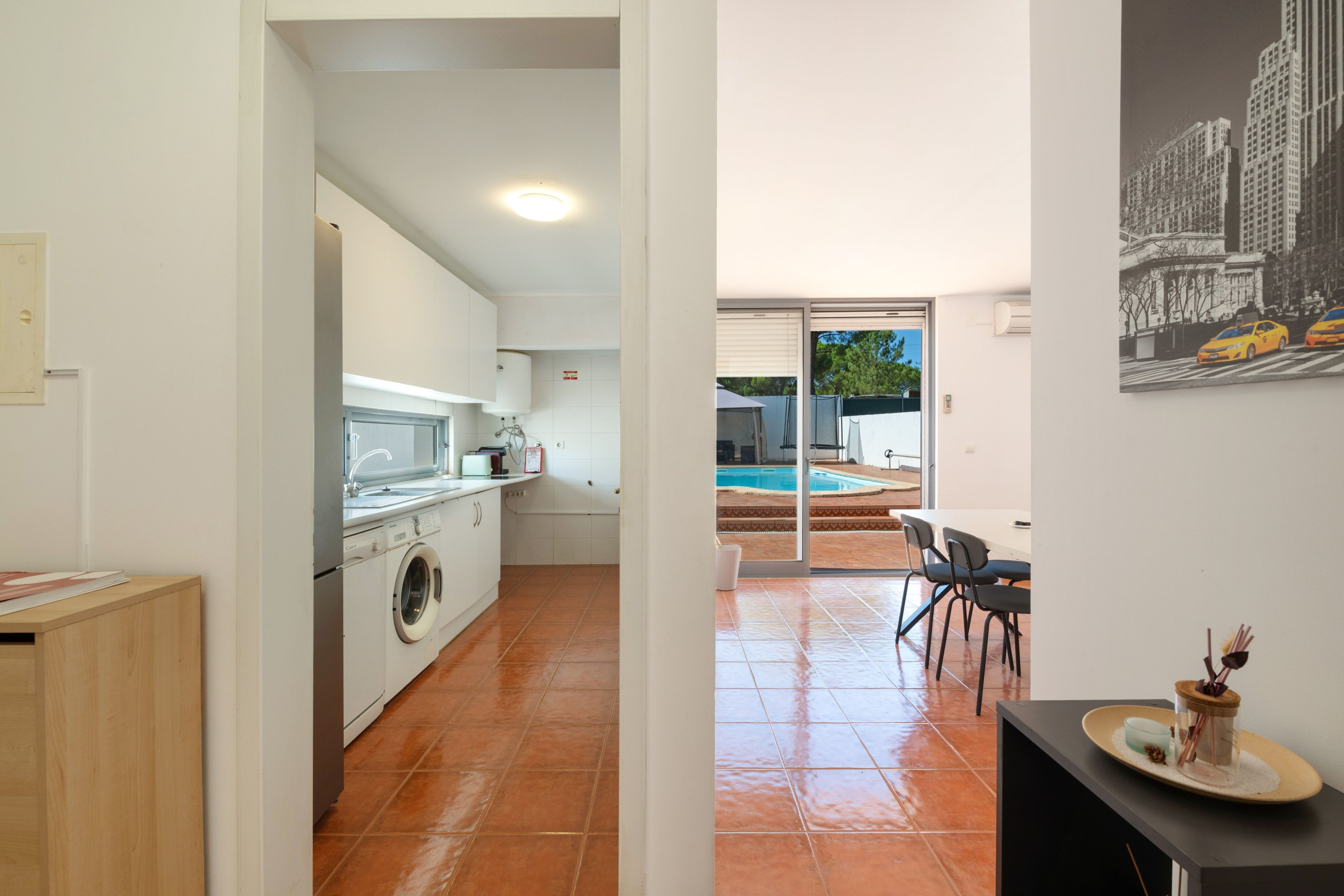 A modern kitchen with a washing machine, a dining area with chairs, and a view of a swimming pool.