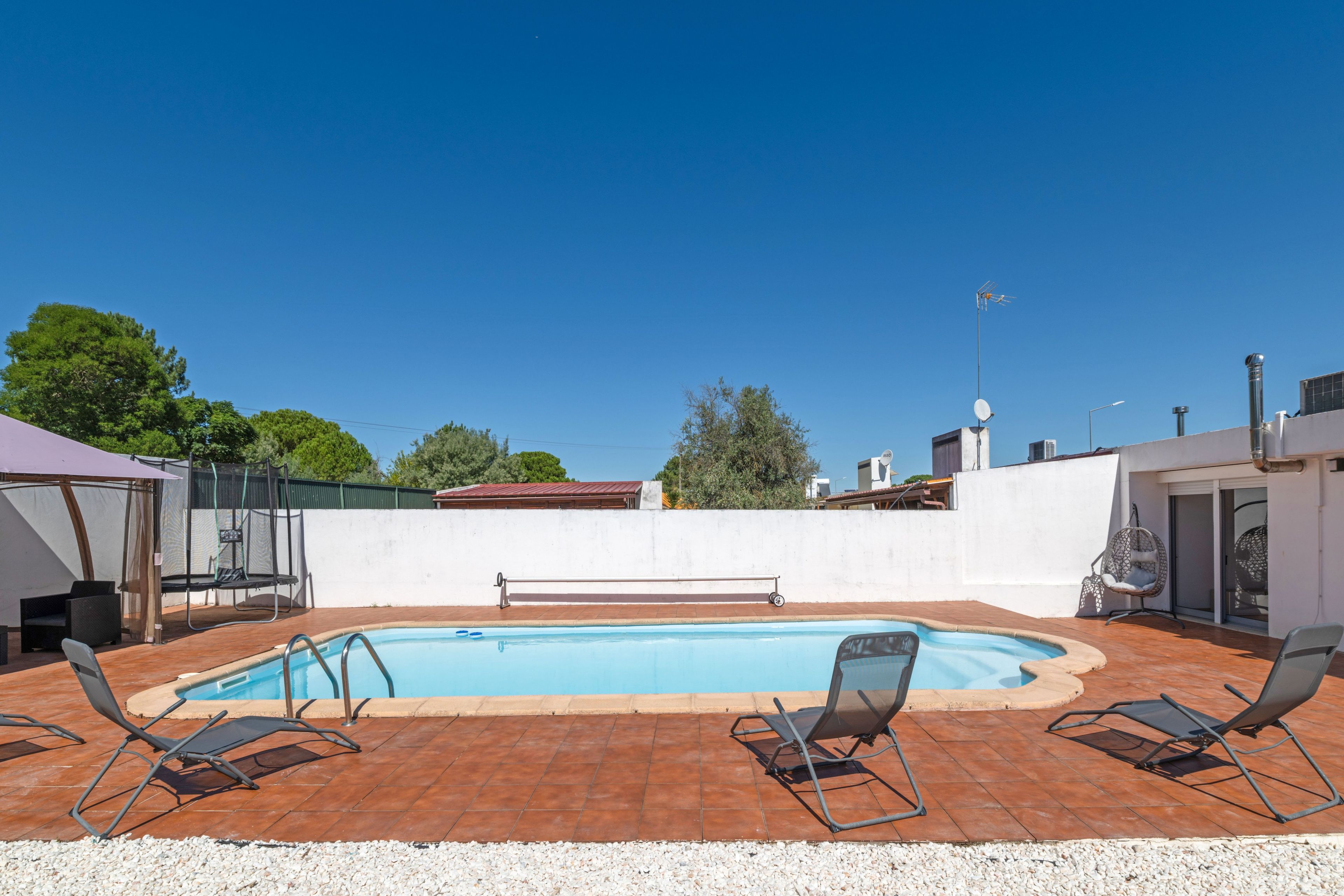 A swimming pool with a tiled deck, surrounded by lounge chairs and a covered seating area.