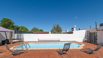 A swimming pool with a tiled deck, surrounded by lounge chairs and a covered seating area.