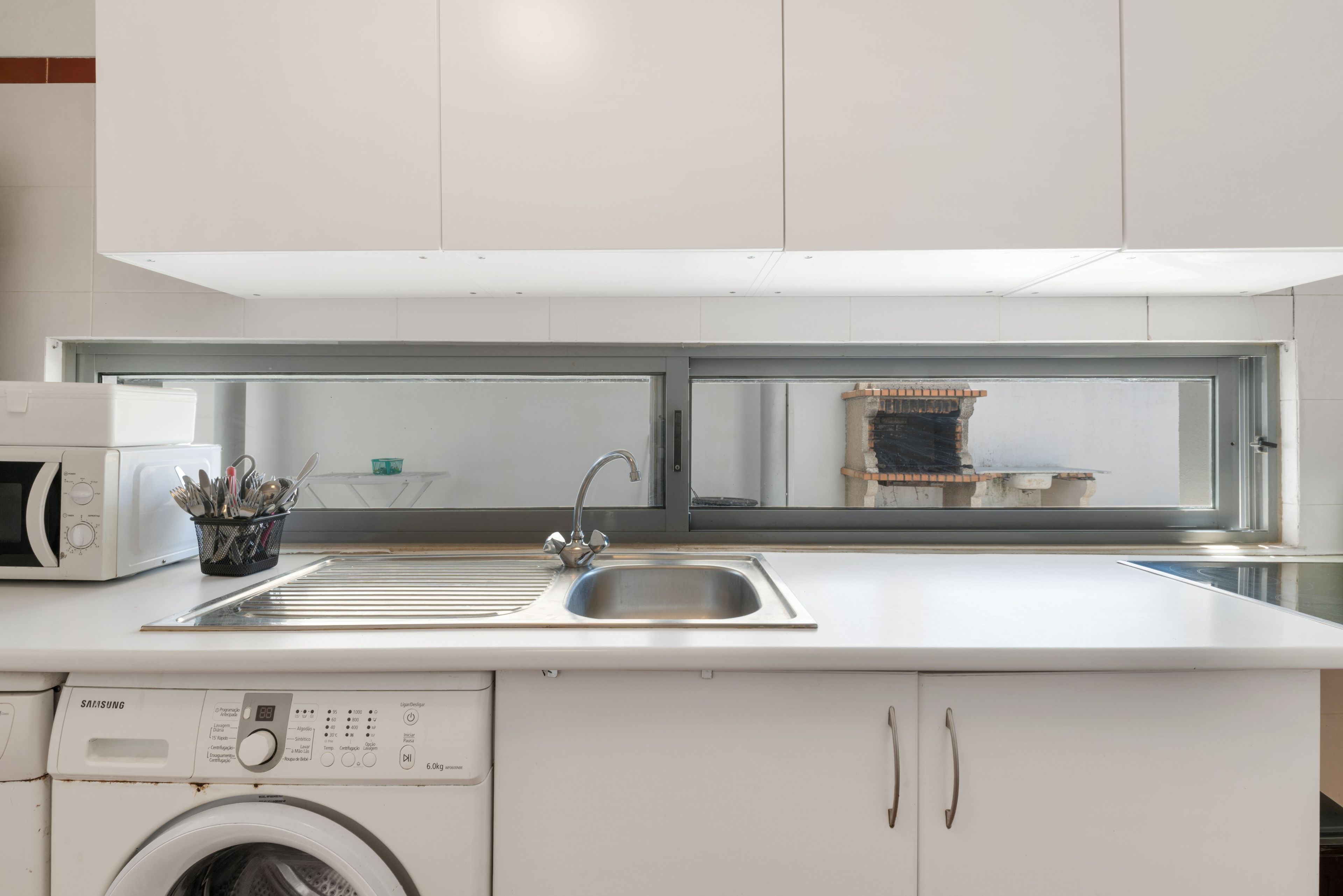 Een moderne keuken met een ingebouwde wasmachine, een roestvrijstalen spoelbak en een raam met uitzicht op een bakstenen gebouw.