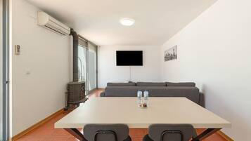 A modern living room with a white table, two chairs, a grey sofa, a flat-screen TV, and a water dispenser.