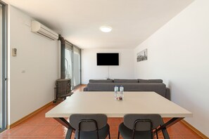 A modern living room with a white table, two chairs, a grey sofa, a flat-screen TV, and a water dispenser.