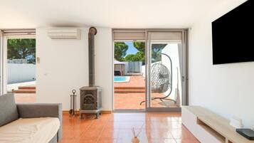 A modern living room with a sofa, a fireplace, a TV, and a view of an outdoor pool area.