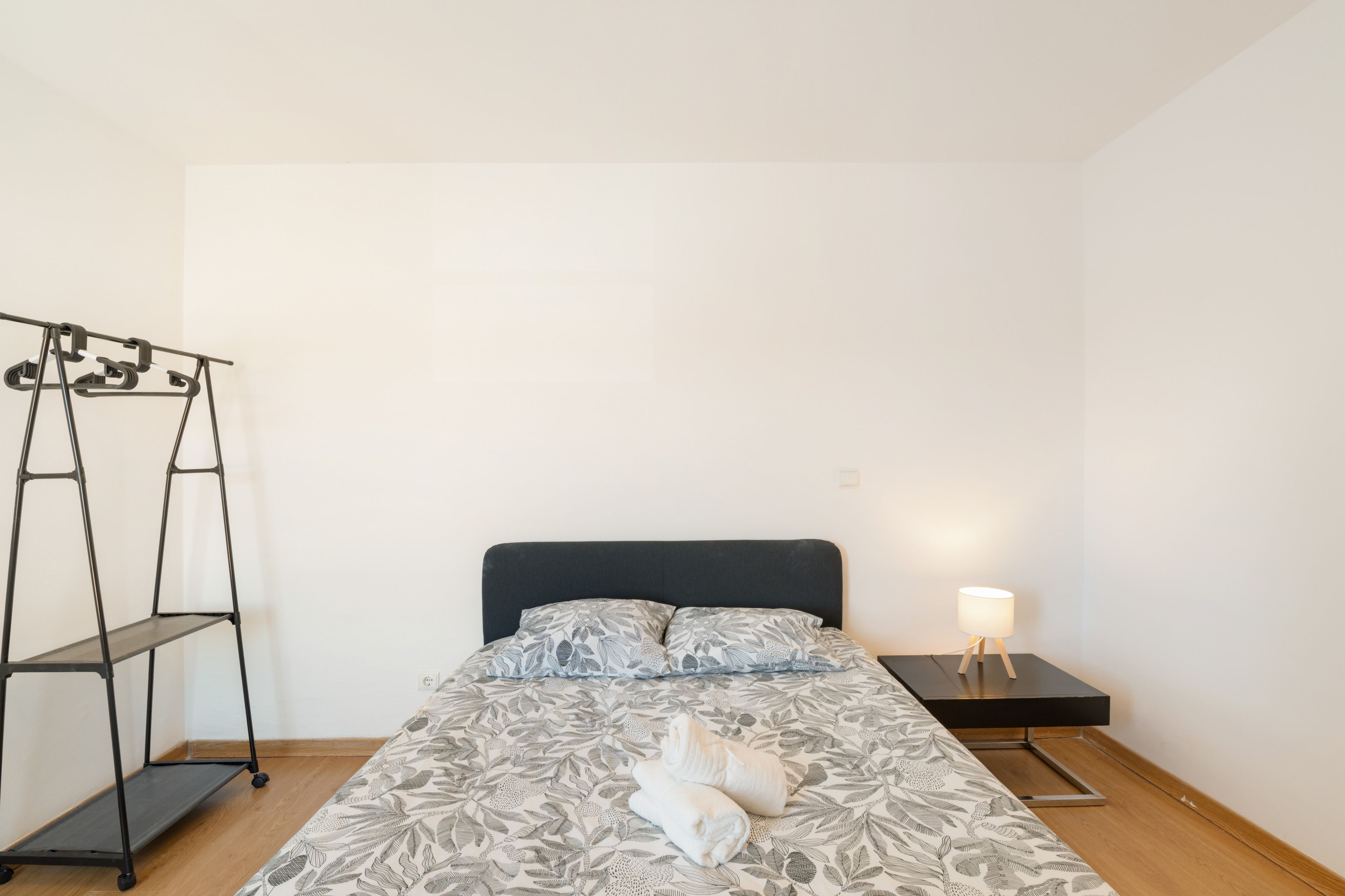 Un dormitorio con cama, mesita de noche, lámpara, armario y estantería.