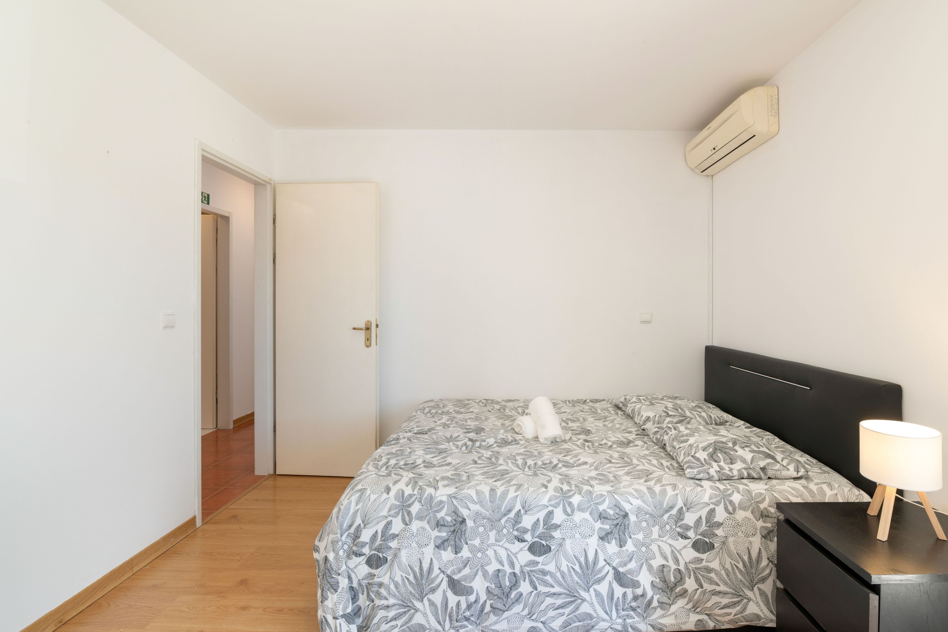 Un dormitorio con una cama, una mesita de noche, una lámpara y un aire acondicionado.