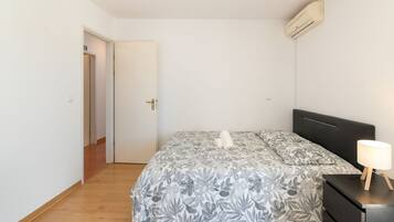 Un dormitorio con una cama, una mesita de noche, una lámpara y un aire acondicionado.