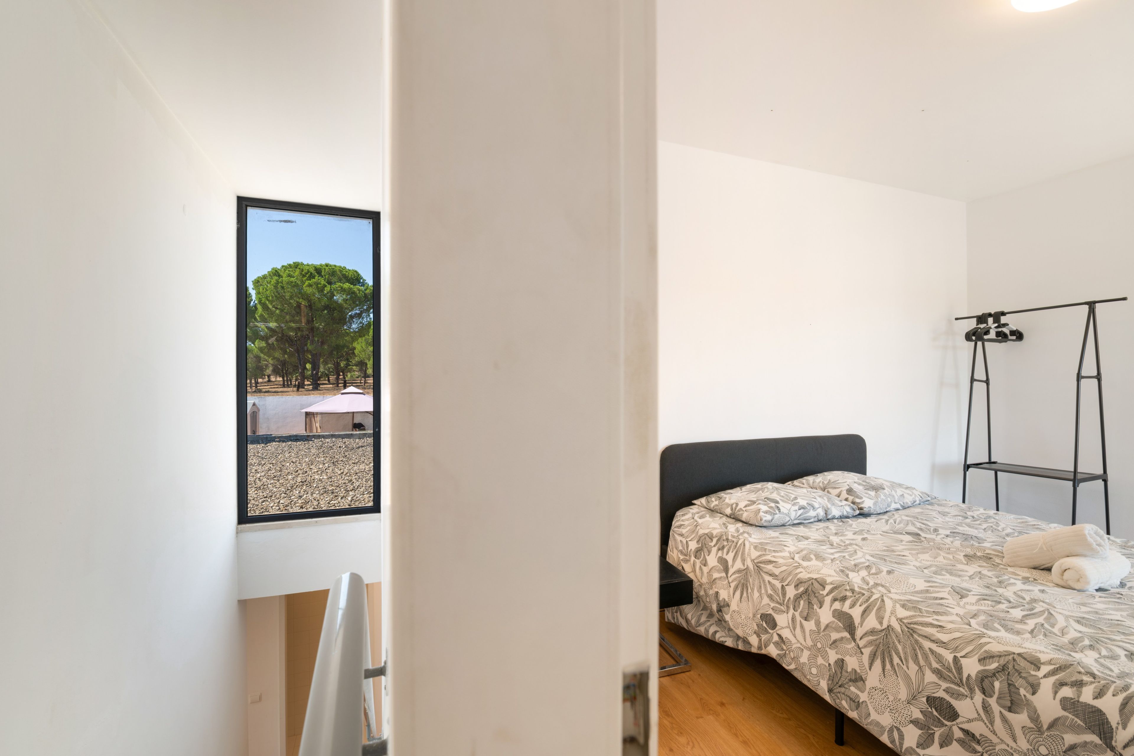 Un dormitorio con una cama, un ventanal con vistas a árboles y un soporte de metal negro.
