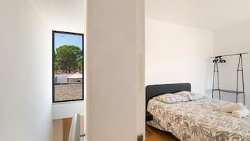 Un dormitorio con una cama, un ventanal con vistas a árboles y un soporte de metal negro.