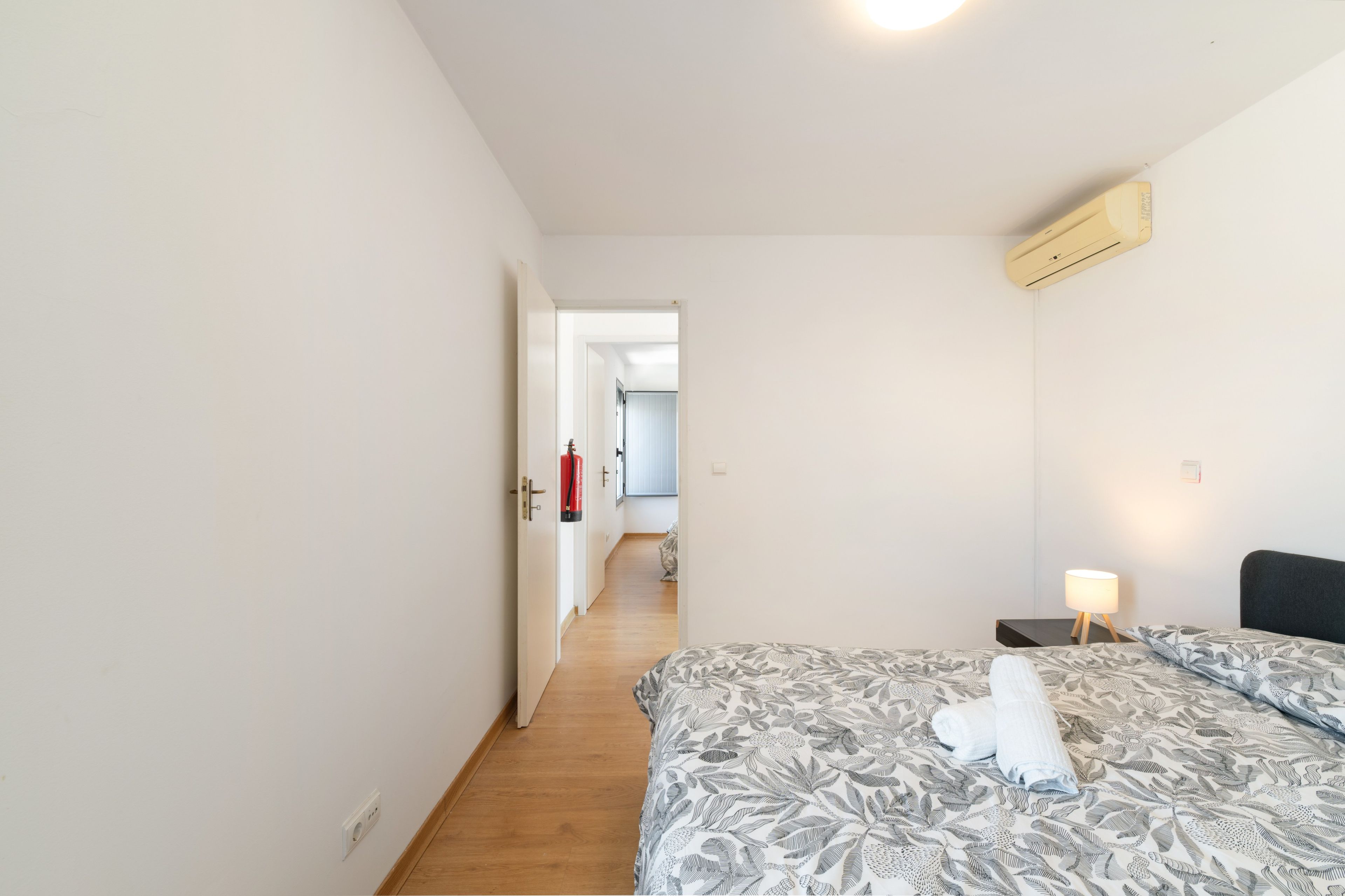 A hotel room with a bed, bedside lamp, and a fire extinguisher.