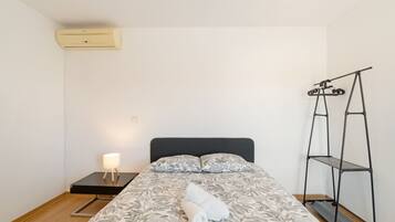 A bedroom with a bed, a nightstand, a lamp, and a wall-mounted air conditioner.