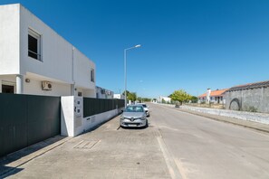 A street with parked cars, a white building with a black fence, and a clear blue sky.