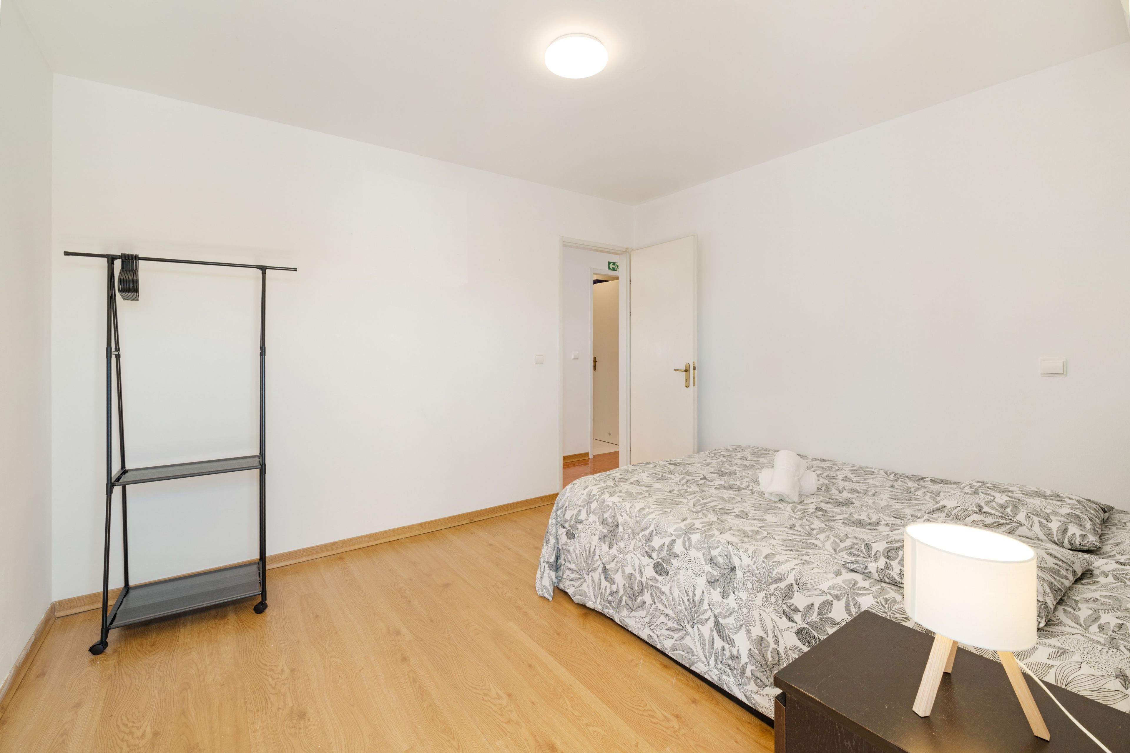 Un dormitorio con cama, mesita de noche con lámpara, armario y puerta que da a otra habitación.