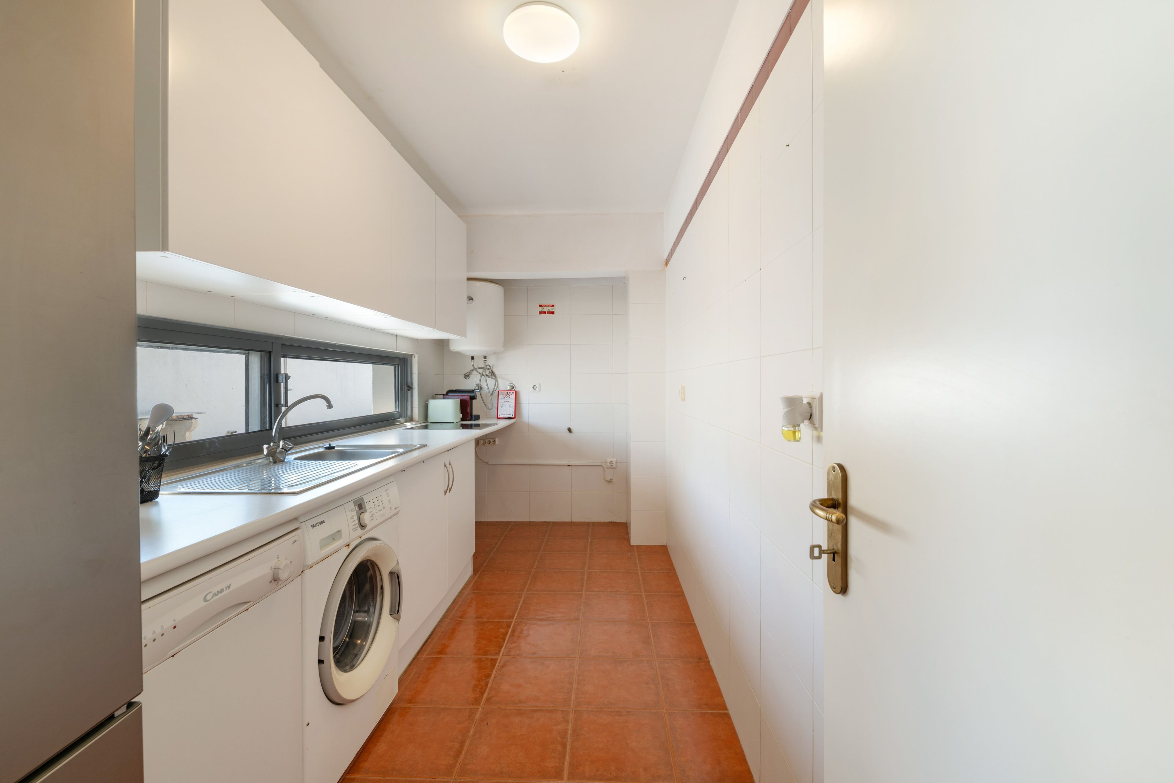 Une cuisine compacte équipée d’un lave-linge, d’un évier et d’un petit plan de travail.